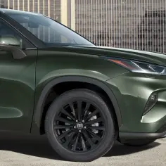 Nowy, zielony Toyota Highlander 2025 z czarnymi felgami prezentuje się elegancko na tle nowoczesnych budynków.