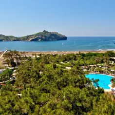 Widok na plażę i morze z wyspami w oddali. Widać basen hotelowy, palmy i sosny. Idealne miejsce na wakacje w Sarigerme.
