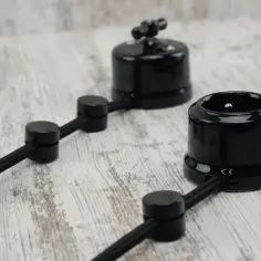 Elegancka instalacja elektryczna natynkowa z czarnymi ceramicznymi elementami: gniazdkiem i wyłącznikiem, na drewnianym tle.