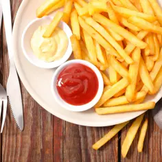 Złociste frytki na talerzu, obok sosy: ketchup i majonez. Idealne dodatki do tego, co pasuje do frytek.