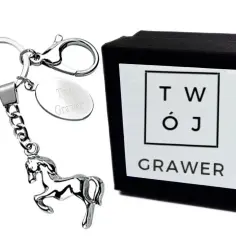 Eleganckie gadżety z koniem: brelok z metalowym koniem i owalną zawieszką z grawerem "Twój Grawer" obok czarnego pudełka z logo "TWÓJ GRAWER".