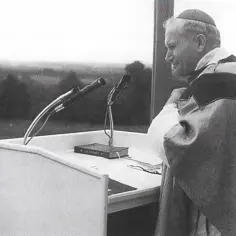 Jan Paweł II przy mównicy, gotów do recytacji wierszy Karola Wojtyły. Tłum słuchaczy w tle.