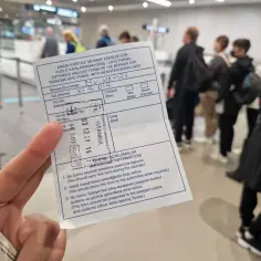Formularz wjazdu/wyjazdu do Turcji dla osób podróżujących na dowód osobisty. W tle widać ludzi w kolejce na lotnisku.