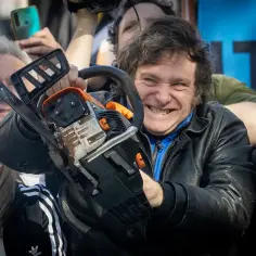 Prezydent Argentyny Javier Milei z uśmiechem trzyma piłę mechaniczną, otoczony przez tłum ludzi.