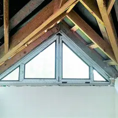 Trójkątne okna w ścianie szczytowej, otoczone drewnianą konstrukcją dachu.