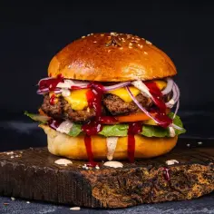Soczyste burgery z grilla, polane sosem, z serem i warzywami, na drewnianej desce.