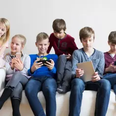 Dzieci na kanapie grają na telefonach i tabletach. Może szukają, jak wyłączyć nadzór rodzicielski bez usuwania konta?
