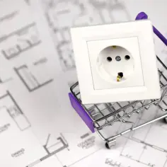 Biały włącznik światła pojedynczy w miniaturowym wózku sklepowym na tle planów architektonicznych.