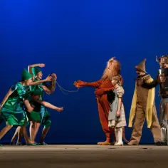 Na scenie musicalu "Czarnoksiężnik z Krainy Oz" tańczący zieloni mieszkańcy spotykają Lwa, Dorotkę, Stracha na Wróble i Blaszane Drzewo.