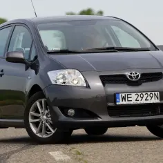 Szary Toyota Auris na drodze. Ten samochód, zasilany sprawnym akumulatorem Toyota Auris, jedzie przez zielone pola.
