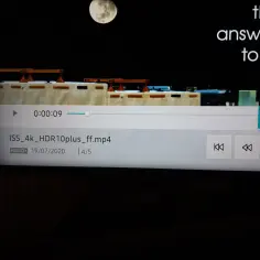 Ekran telewizora z interfejsem odtwarzacza wideo, widoczny fragment filmu z ISS i księżycem.
