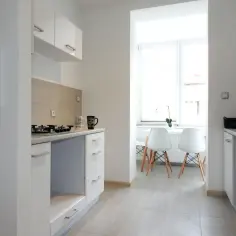 Nowoczesna kuchnia z białymi meblami, płytkami na ścianie i dwoma białymi krzesłami przy oknie.