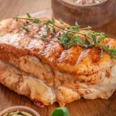 Soczysty filet z indyka, pieczony z ziołami, idealny na obiad. Obok pomidorki i miseczka z ziarnami.