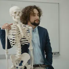 Nauczyciel z kręconymi włosami prezentuje szkielet, symbolizując nową erę biologii na czasie.