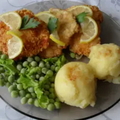 Pyszny antrykot z kurczaka w panierce, podany z puree ziemniaczanym i zielonym groszkiem, ozdobiony plasterkami cytryny.