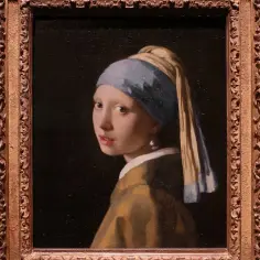 Dziewczyna z perłą, w błękitnym turbanie i żółtej szacie, spogląda przez ramię. Jej spojrzenie jest intrygujące, a jedyna perła w uchu błyszczy.