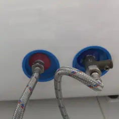 Dwa przyłącza wodne bojlera z wężami i zaworem.