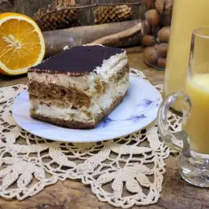 Słodki deser tiramisu, połówka pomarańczy i kieliszek likieru pomarańczowego na drewnianym blacie.