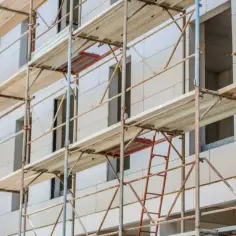 Rusztowanie wokół budynku, z drewnianymi platformami i metalowymi elementami. Pomaga to zrozumieć, jak obliczyć ilość rusztowania potrzebną do budowy.