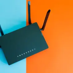 Czarny router z antenkami na tle niebiesko-pomarańczowym. Dowiedz się, jak to urządzenie pomaga w temacie: jak secure home wifi.