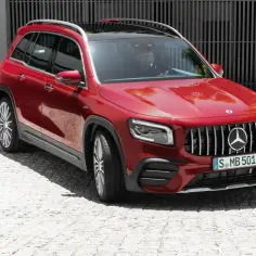 Czerwony Mercedes 7 osobowy GLB AMG z kierowcą za kierownicą, zaparkowany na brukowanej nawierzchni.