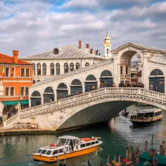 Most Rialto Bridge w Wenecji, z łodziami na kanale i turystami na moście. Czy Wenecja jest bezpieczna? Tak, wygląda na to, że turyści czują się tu swobodnie.