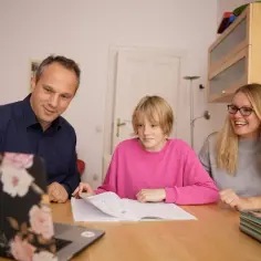 Rodzina uczy się matematyki. Ojciec i matka pomagają córce, która przegląda zeszyt. Zastanawiasz się, ile zarabia korepetytor matematyki?