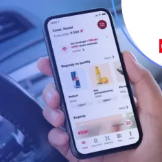 Dłoń trzyma smartfon z aplikacją ORLEN Pay, pokazującą punkty VITAY i nagrody. Kierownica samochodu w tle.