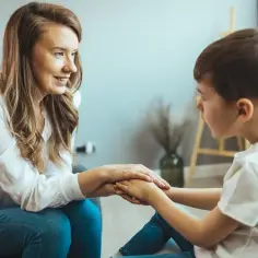 Kobieta i chłopiec trzymają się za ręce, wspierając się nawzajem. Może to symbolizować wydłużenie etapu edukacyjnego, gdzie wsparcie jest kluczowe.