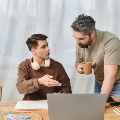 Ojciec rozmawia z synem, pokazując mu coś na laptopie. Rozmowa o tym, jak zmotywować dziecko do nauki, przebiega w przyjaznej atmosferze.