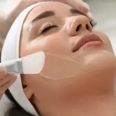 Kobieta z opaską na głowie otrzymuje peeling twarzy za pomocą silikonowej szpatułki.