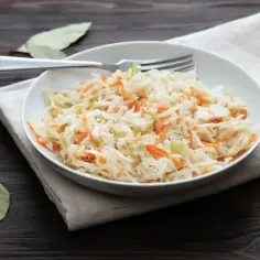 Chrupiąca surówka z białej kapusty jak w restauracji, z marchewką i przyprawami, na talerzu z widelcem.