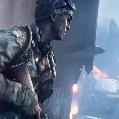 Żołnierz w czapce i goglach, gotowy do akcji w jednej z najbardziej realistycznych gier fps. W tle płonące ruiny i dym.
