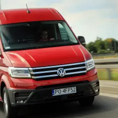 Czerwony VW Crafter pędzi autostradą. Kierowca w okularach prowadzi auto, które jest w ruchu.