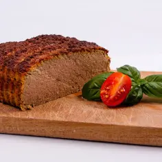 Pokrojony pasztet na desce z pomidorkiem koktajlowym i bazylią.