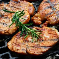 Soczyste plastry karkówki, idealnie przypieczone na grillu, z gałązką rozmarynu. To efekt doskonałej marynaty do karkówki na grilla.