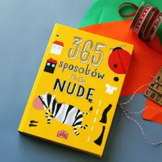 Żółta książka "365 sposobów na nudę" z zebrą i biedronką, obok kolorowy papier, wstążki i drewniane literki. Idealna na nudne dni.