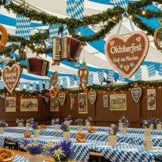 Wnętrze namiotu na Oktoberfest w Monachium. Wiszące precle, akordeony i serca z napisem "Oktoberfest". Stoły przykryte niebiesko-białymi obrusami, ozdobione kwiatami i beczką chmielu.