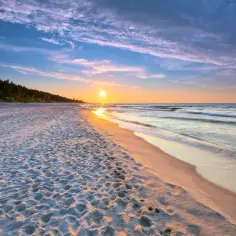 Piękny zachód słońca na plaży, idealny na tani weekend nad morzem dla dwojga. Ślady na piasku prowadzą do spokojnego morza.