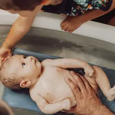 Delikatna kąpiel noworodka w wanience. Starsze dziecko z ciekawością obserwuje maluszka, a rodzice troskliwie go kąpią.