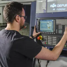 Operator CNC przy panelu sterowania maszyny. Dobra praca to wysokie operator cnc zarobki.