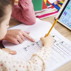 Dziecko z pomocą nauczyciela ćwiczy pisanie liter, by pokonać dysleksję u dzieci. Tablet z alfabetem wspiera naukę.