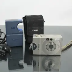 Aparat fotograficzny Canon IXUS służy do robienia zdjęć. W zestawie ładowarka i etui.