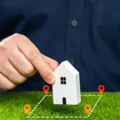 Działka z warunkami zabudowy i jej sprzedaż a VAT. Ręka trzyma model domu na tle zielonej trawy z zaznaczonymi granicami działki.