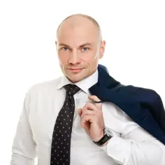 Łysy mężczyzna w białej koszuli i krawacie z kropkami, z marynarką na ramieniu.