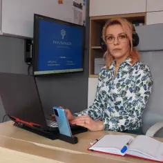 Kobieta w słuchawkach siedzi przy biurku, pracuje na laptopie, obok telefon i notatnik.