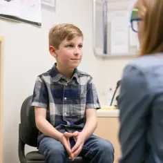 Chłopiec z ADHD siedzi na krześle, rozmawiając z terapeutką.