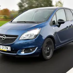 Niebieski Opel Meriva B 1.4 Turbo pędzi po drodze, otoczony jesiennym krajobrazem.