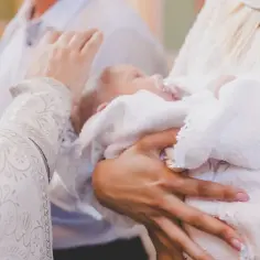 Dziecko owinięte w biały ręcznik, trzymane na rękach. Może to prezent od cioci na chrzest.