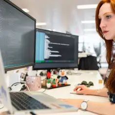 Programistka z rudymi włosami pracuje przy komputerze, pisząc kod w środowisku .NET Framework.